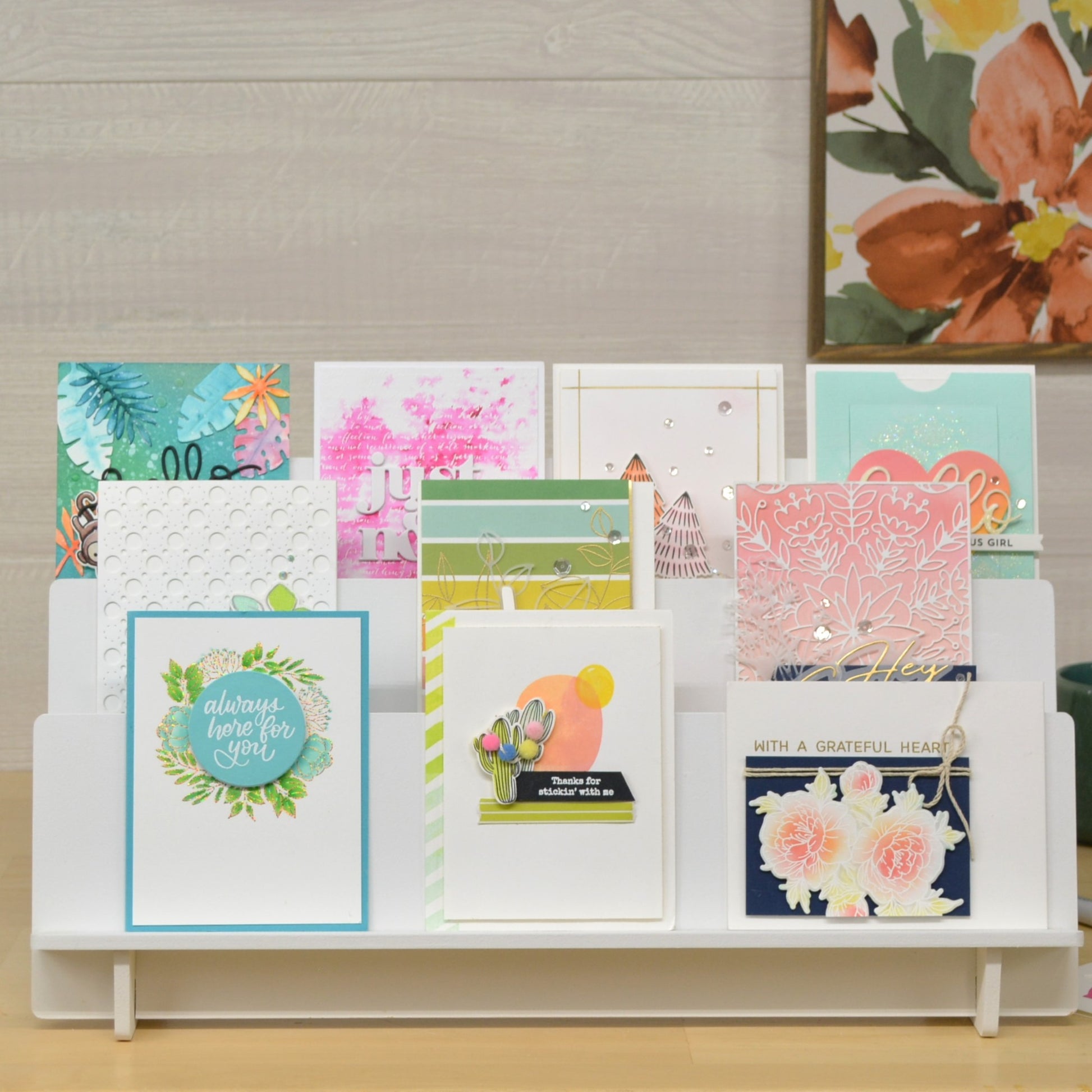 front view of greeting cards in a white three level display stand on a wood table top