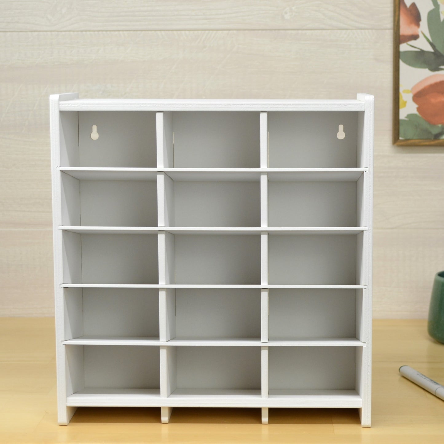 front view of a white marker organizer with fifteen cubbies and keyholes in the back for wall mounting